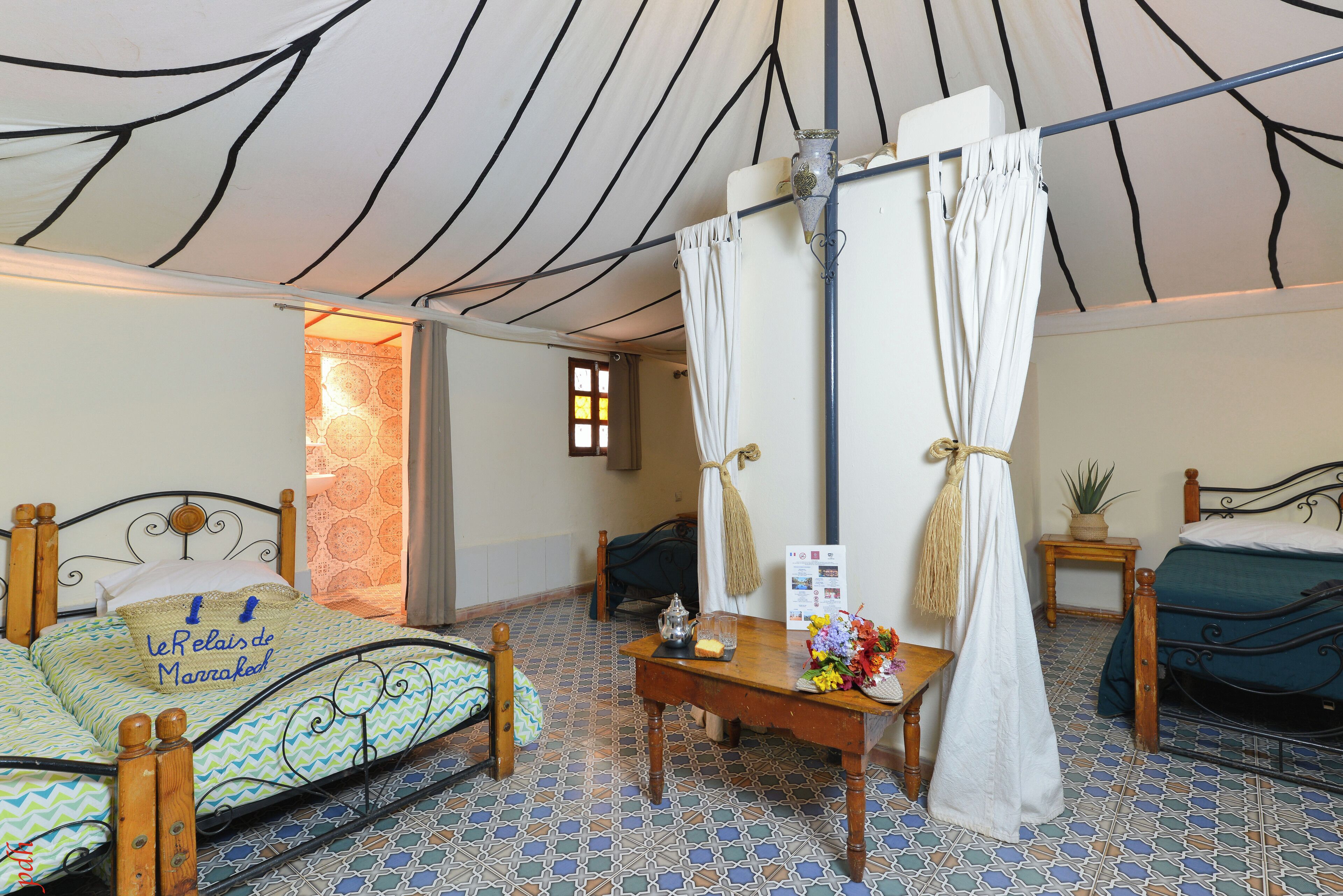 Een tent met een bed, een tafel met een bloevas en een kleine tafel met een plant.