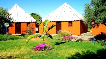 Dois edifícios com telhados brancos e paredes laranja, rodeados por jardins bem cuidados e um céu azul límpido.