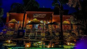A building with outdoor seating and umbrellas, a pool area with geometric light patterns, and a night sky with a visible moon. - Le Relais De Marrakech (Marrakech)