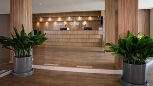 A reception area with a wooden reception desk, a receptionist, and two potted plants. - Zornica Residence (Sunny Beach)