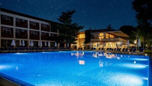 A swimming pool with lounge chairs and umbrellas, a building with multiple floors and balconies, and a night sky with stars. - Zornica Residence (Sunny Beach)