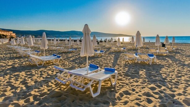 A beach with rows of sun loungers and umbrellas, a clear sky, and a calm sea in the background. - Zornica Residence (Sunny Beach)
