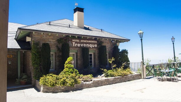 A hotel named Trevenque with a stone facade, outdoor seating area, and a clear blue sky. - Aparthotel Trevenque (Monachil)