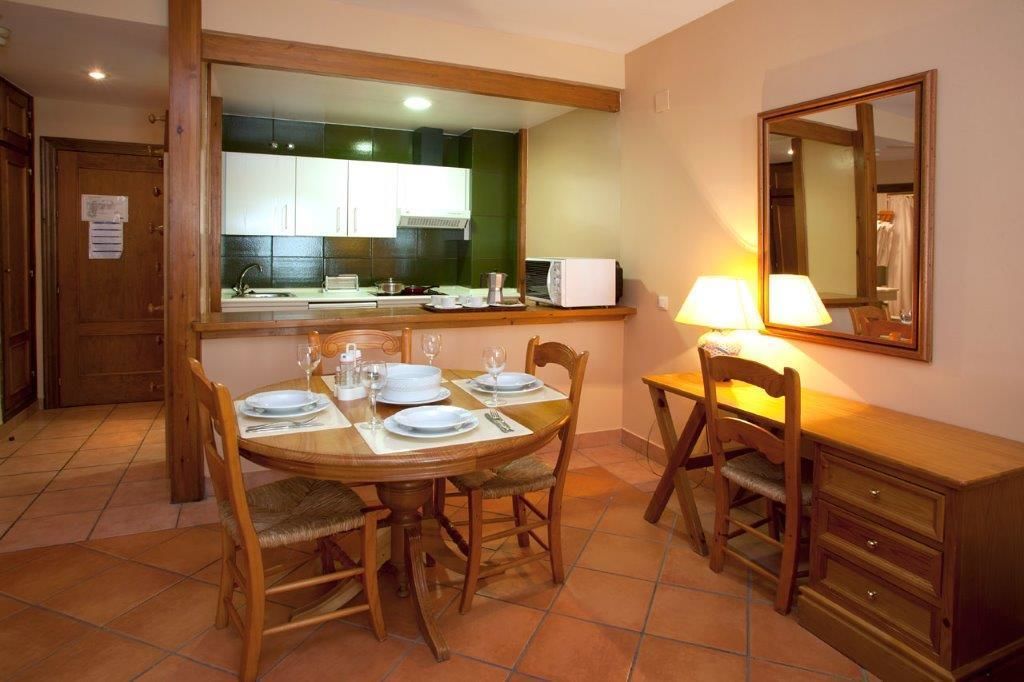 A dining area with a round table set for four, wooden chairs, a small cabinet, and a mirror on the wall.