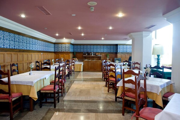 Un comedor con varias mesas y sillas, una cocina al fondo y paredes con diseño.
