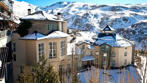 Un bâtiment enneigé, doté de nombreuses fenêtres, avec une chaîne de montagnes en arrière-plan.