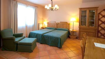 A hotel room with two beds, a green armchair, a wooden cabinet, and a dining table.