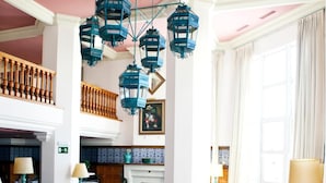 Un hall d’entrée spacieux avec des fauteuils rouges, une cheminée, des lanternes bleues suspendues et une grande fenêtre avec des rideaux.