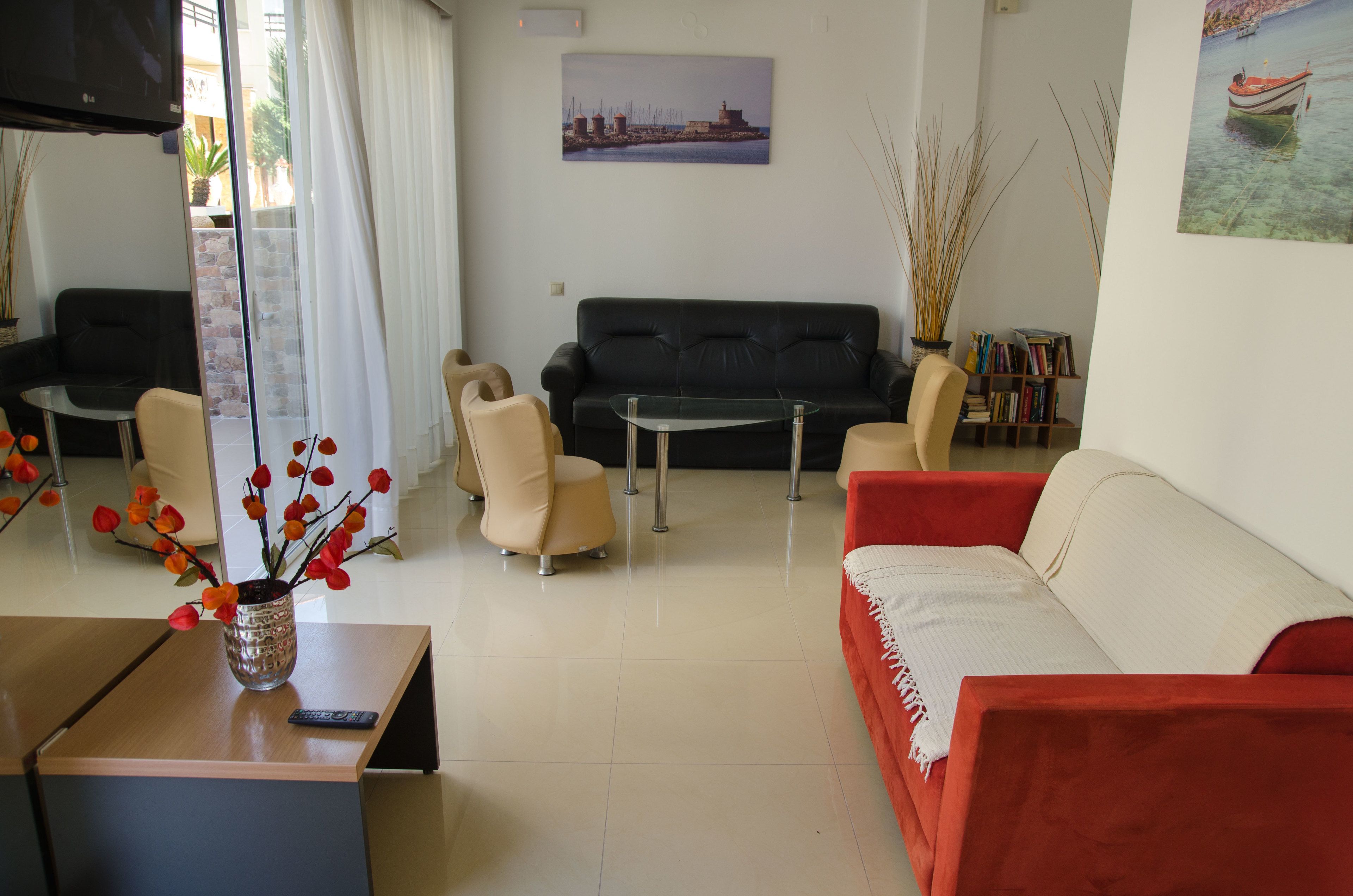Ein Wohnzimmer mit einer schwarzen Couch, einer roten Couch, einem beigen Sessel und einem Glastisch. An der Wand hängt ein Gemälde, und ein Bücherregal ist mit Büchern gefüllt.