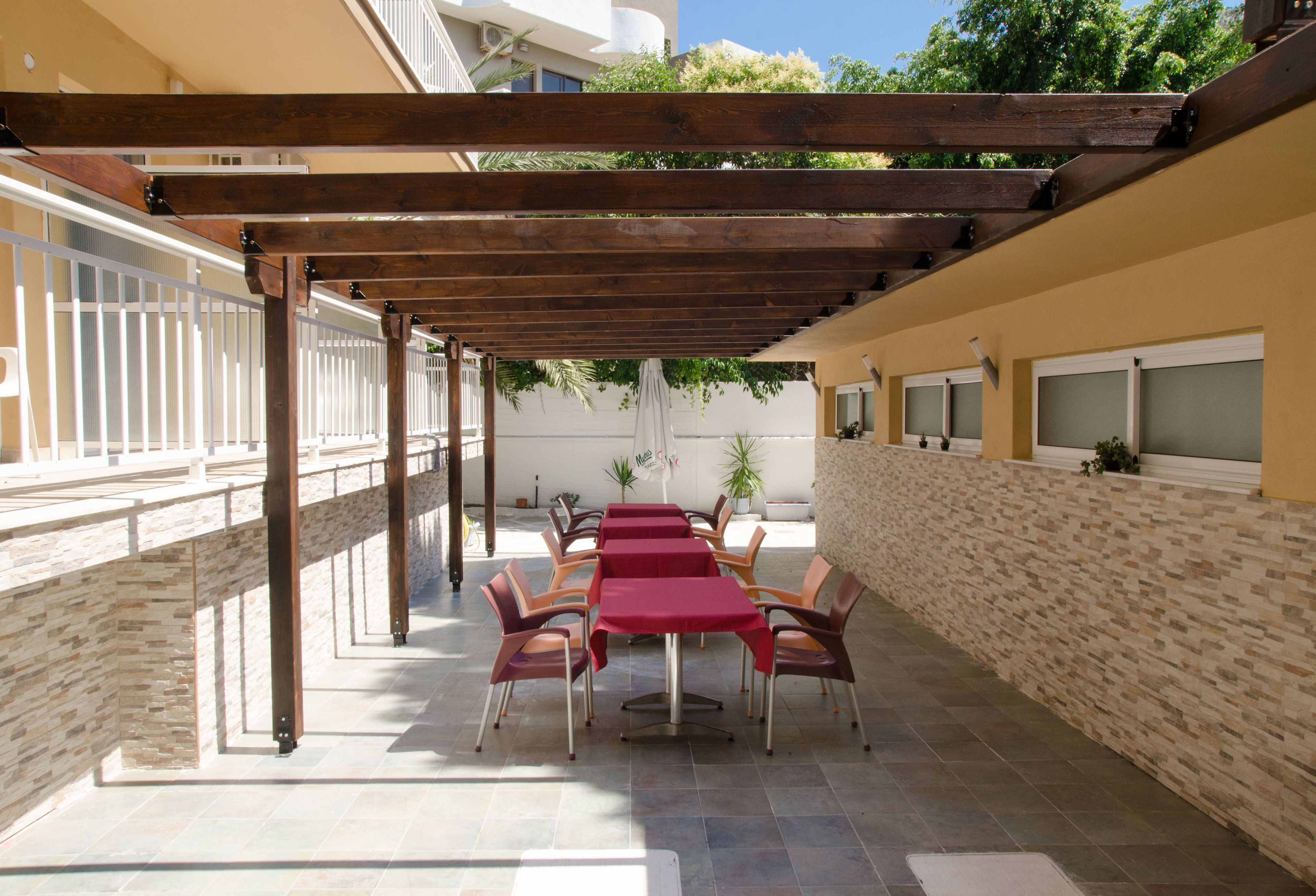 An outdoor patio with a wooden pergola, stone walls, and a row of tables and chairs.