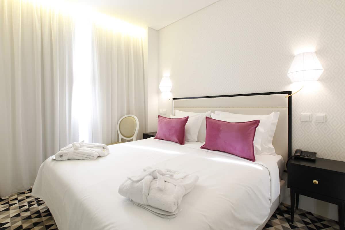 A hotel room with a large bed, white linens, two pillows, a bedside table with a phone, and a nightstand with a lamp.