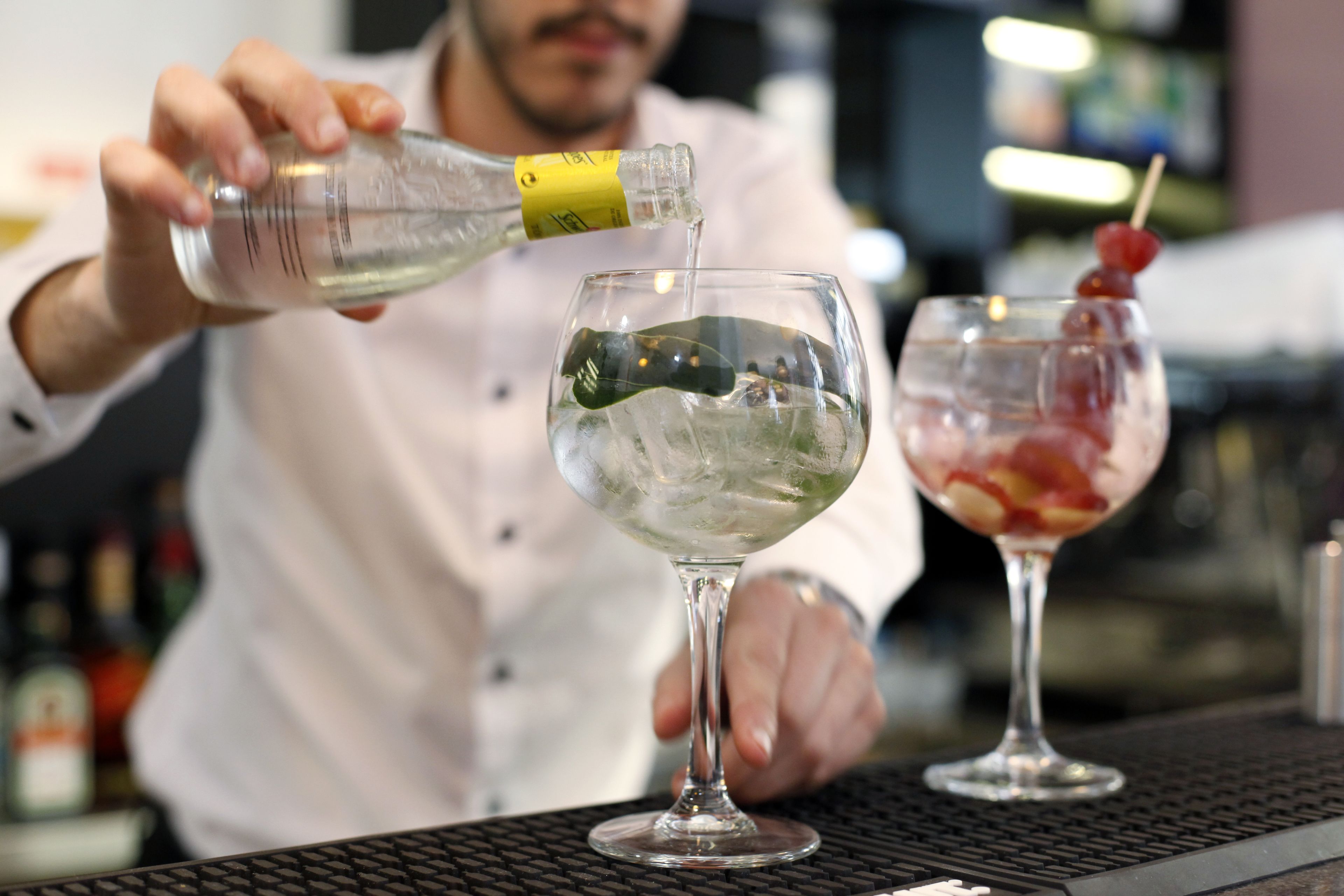 Een barman giet een heldere vloeistof in een glas met ijs en een kers.