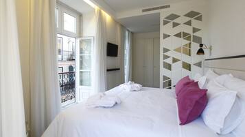 Een hotelkamer met een groot bed, witte lakens, uitzicht op een balkon en een wand met een geometrisch patroon.