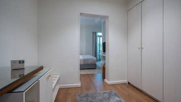 A hotel room with a glass-top desk, a wardrobe, and a bed in the background.
