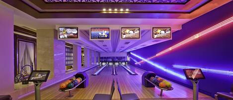 A bowling alley with multiple lanes, a seating area, and a ceiling with decorative patterns.