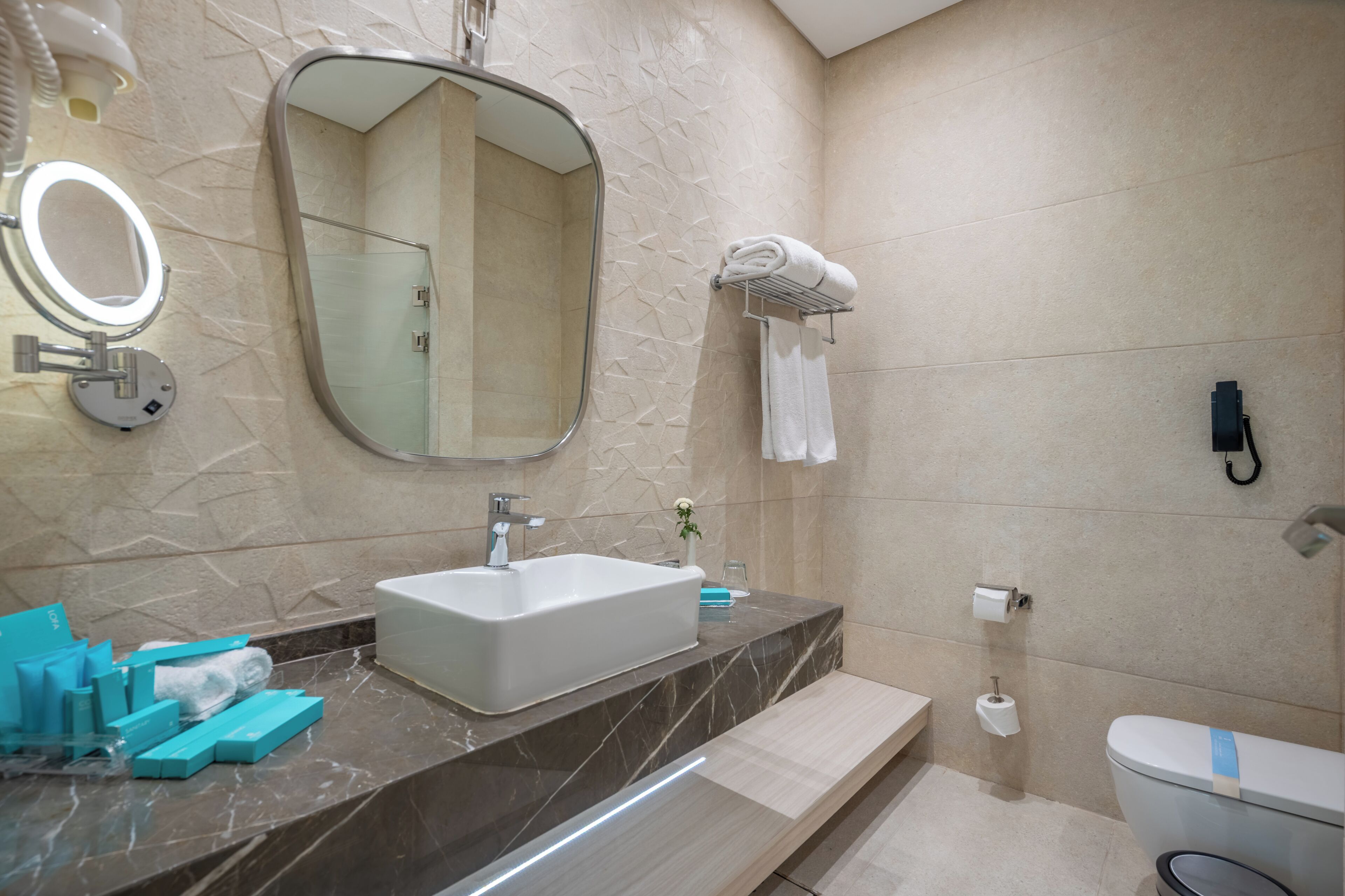 Un baño moderno con lavamanos de mármol, un espejo grande, cabina de ducha de vidrio, inodoro y perchero para toallas.