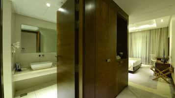 A modern hotel room with a large wooden wardrobe, a white sink, and a bed with a white duvet.