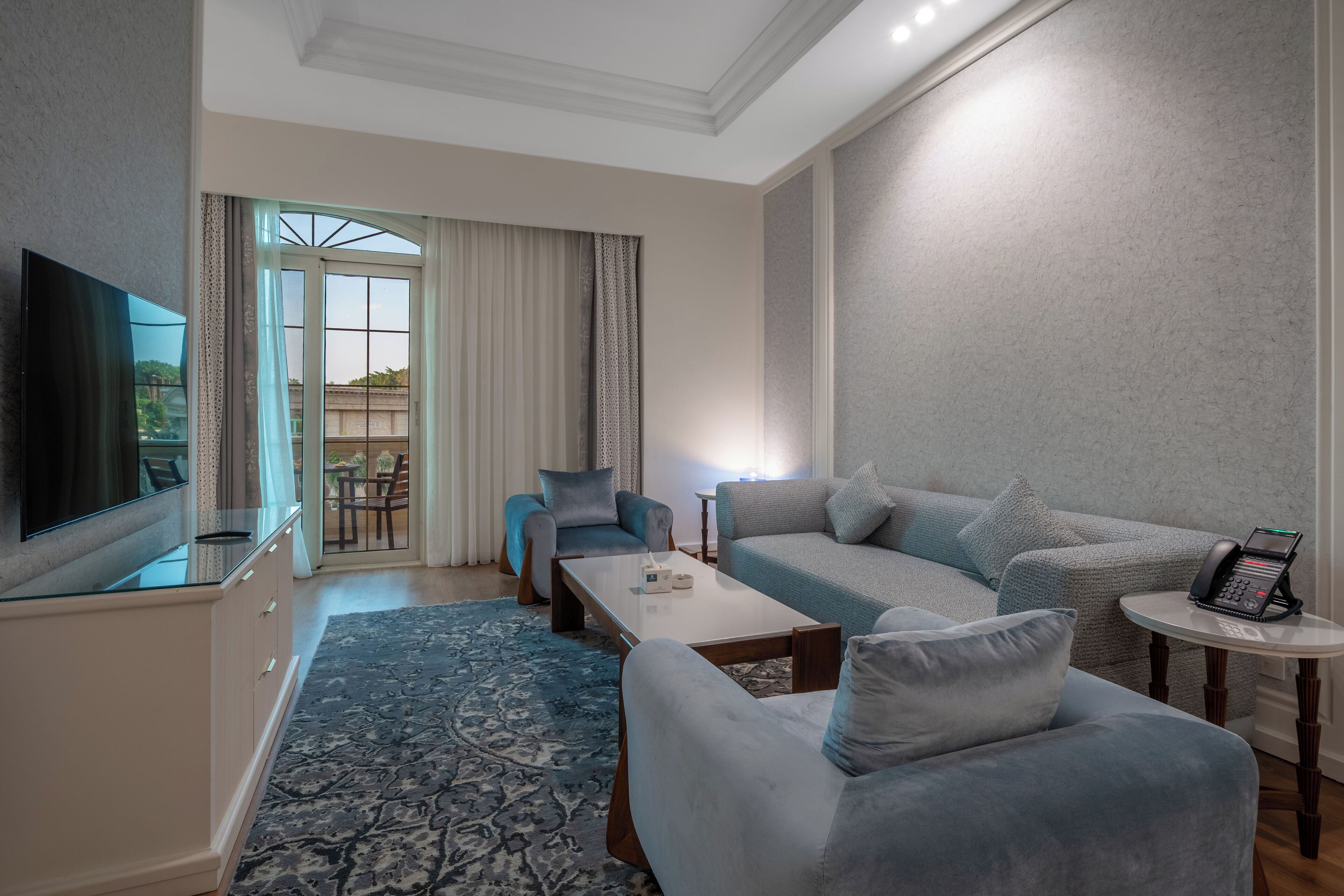 Una sala de estar moderna con un sofá, sillones, una mesa de centro, un televisor y un teléfono sobre una mesita auxiliar.