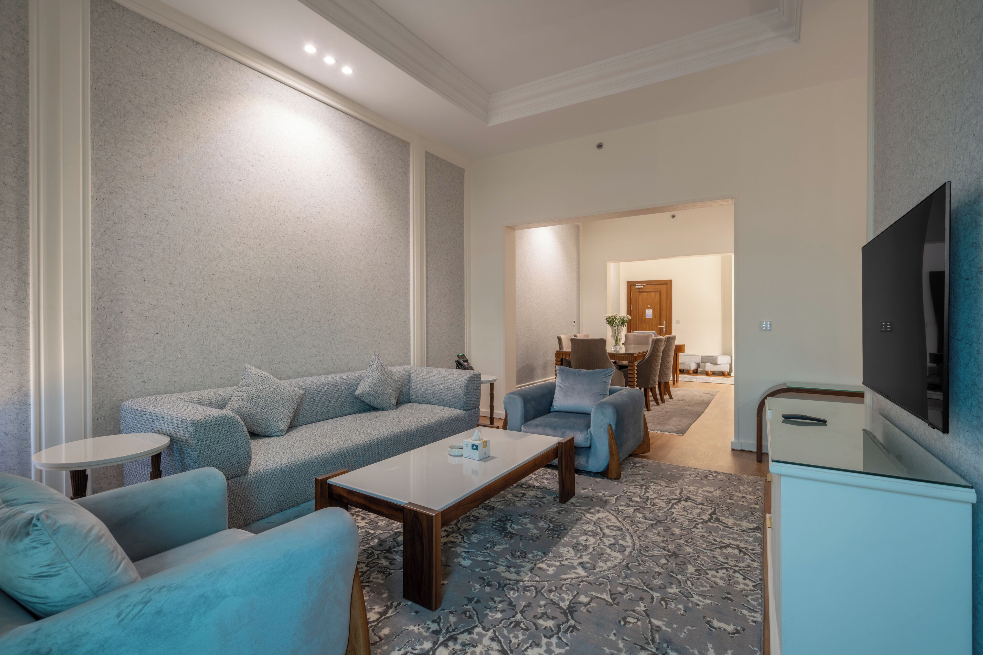 A modern living room with a sofa, armchairs, a coffee table, and a flat-screen TV.