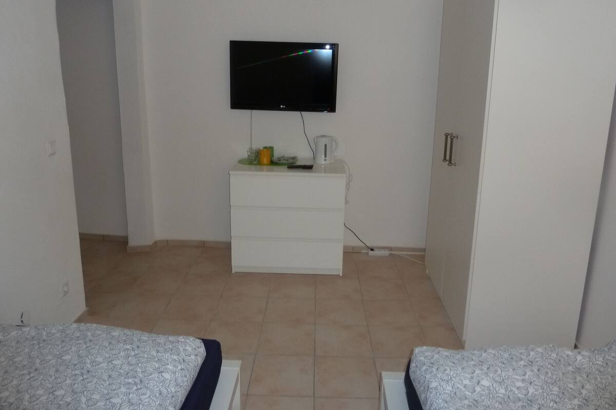 A hotel room with a flat-screen TV mounted on the wall, a white dresser, and two beds with patterned bedding.