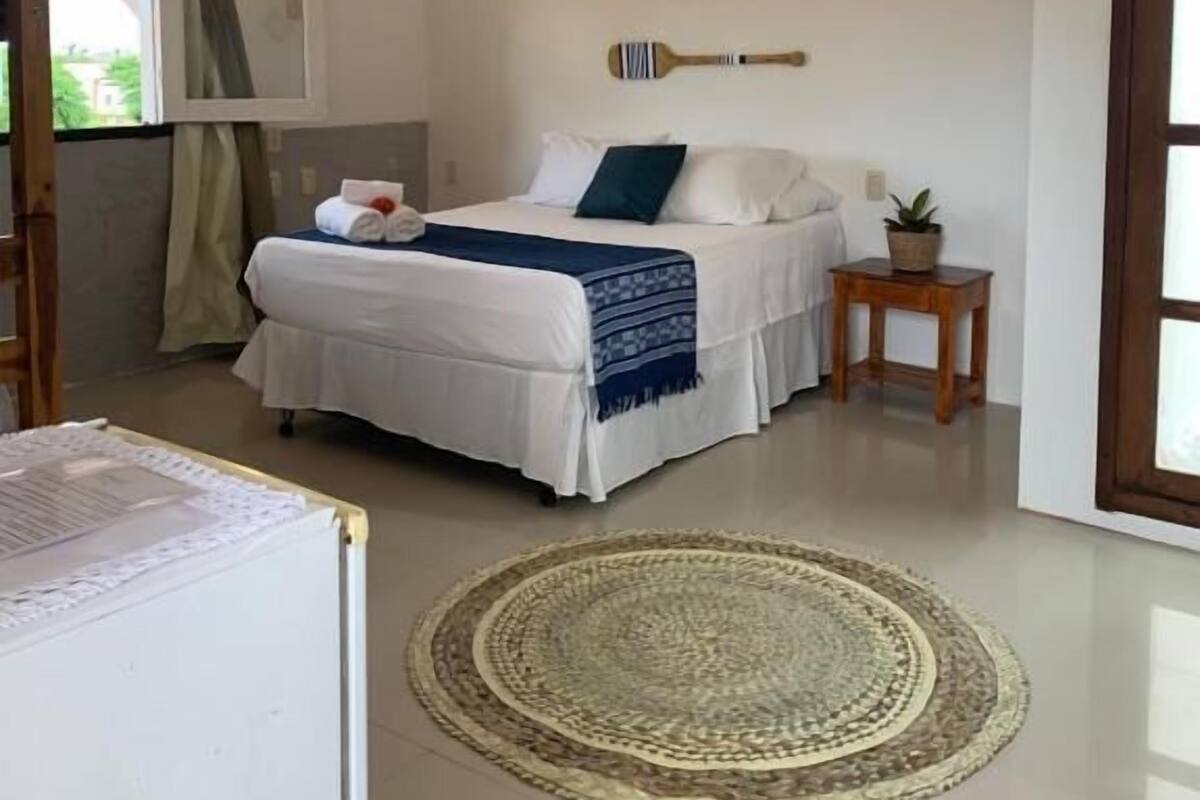 Un dormitorio con cama, una mesita de noche de madera, un cuadro con un pez enmarco y una ventana con cortinas.