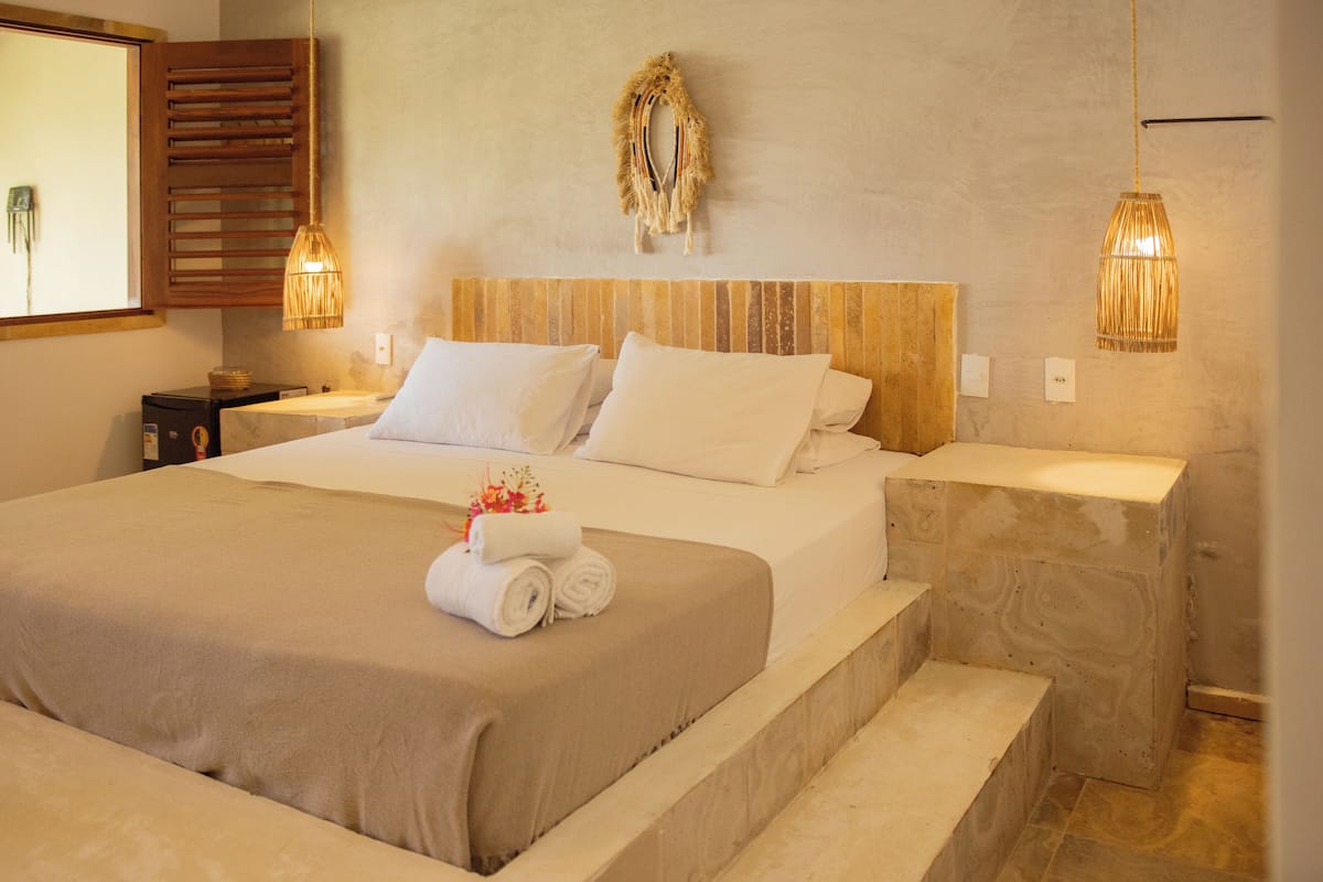 Una habitación de hotel elegante con una cama grande, dos mesitas de noche, un cabecero con una guirnalda decorativa y dos lámparas colgantes.