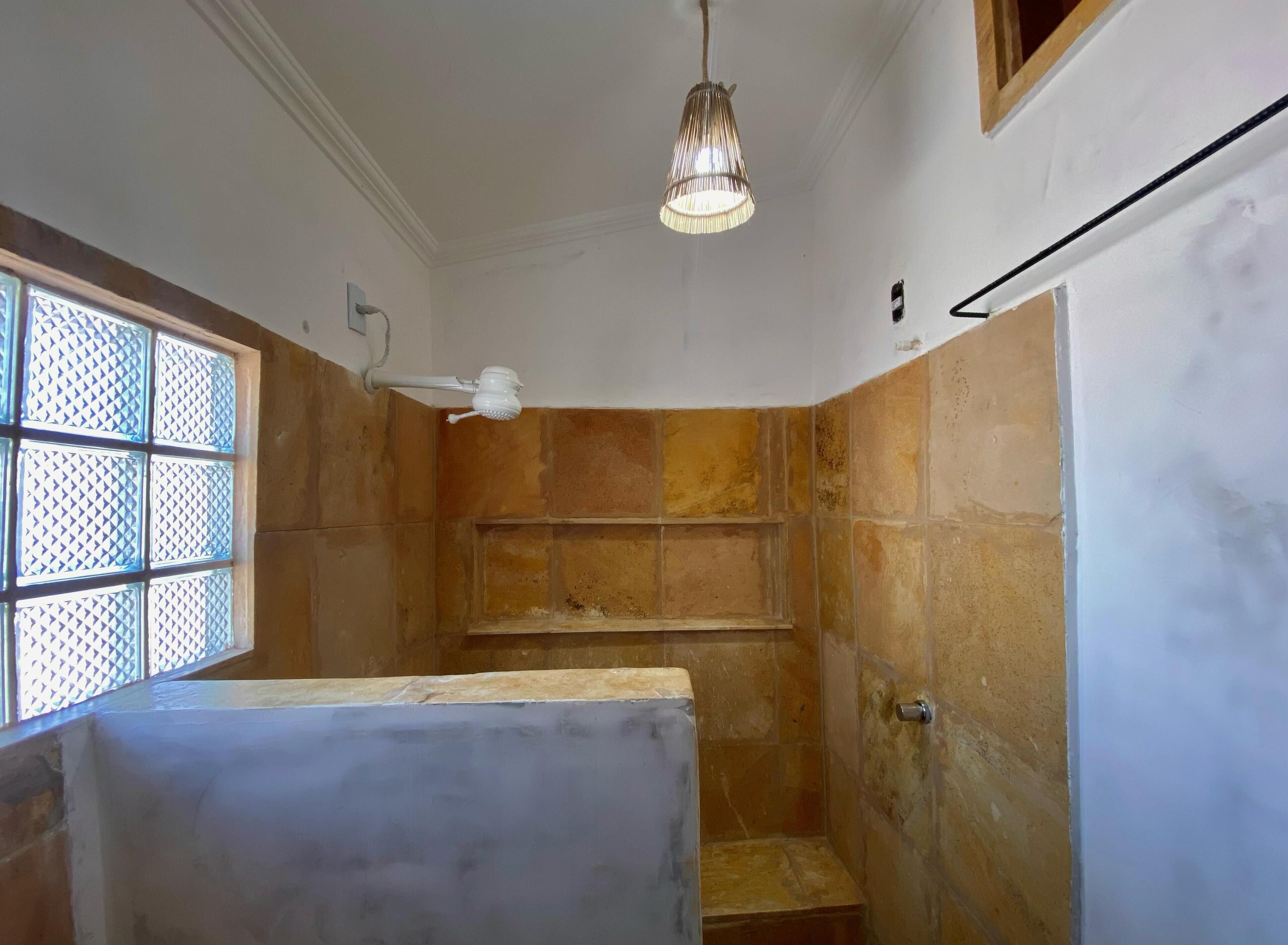 A bathroom with a shower, tiled walls, a window with a grid pattern, and a hanging light fixture.