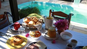 Una tavola imbandita con prodotti per la colazione, tra cui pane, frutta e caffè, vicino a una piscina.