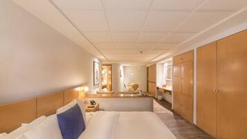 Quarto de hotel com uma cama grande, armário de madeira, uma mesa com cadeira e uma área de banheiro pequena.