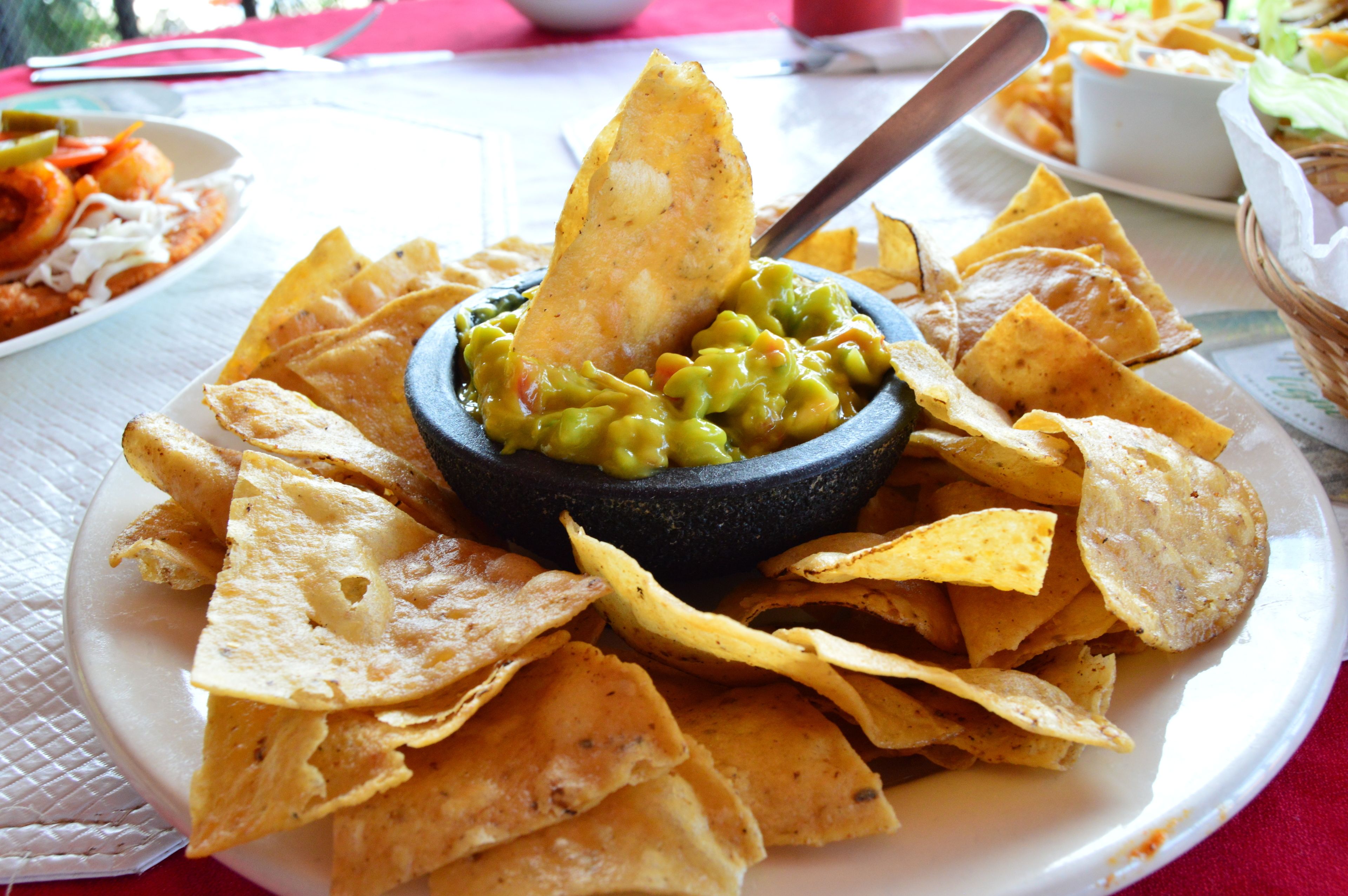 A plate of nachos with a bowl of guacamole and a tortilla chip.
