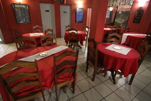 A restaurant with multiple tables and chairs, red tablecloths, and a tiled floor. - Rolson Hotel (San Ignacio)