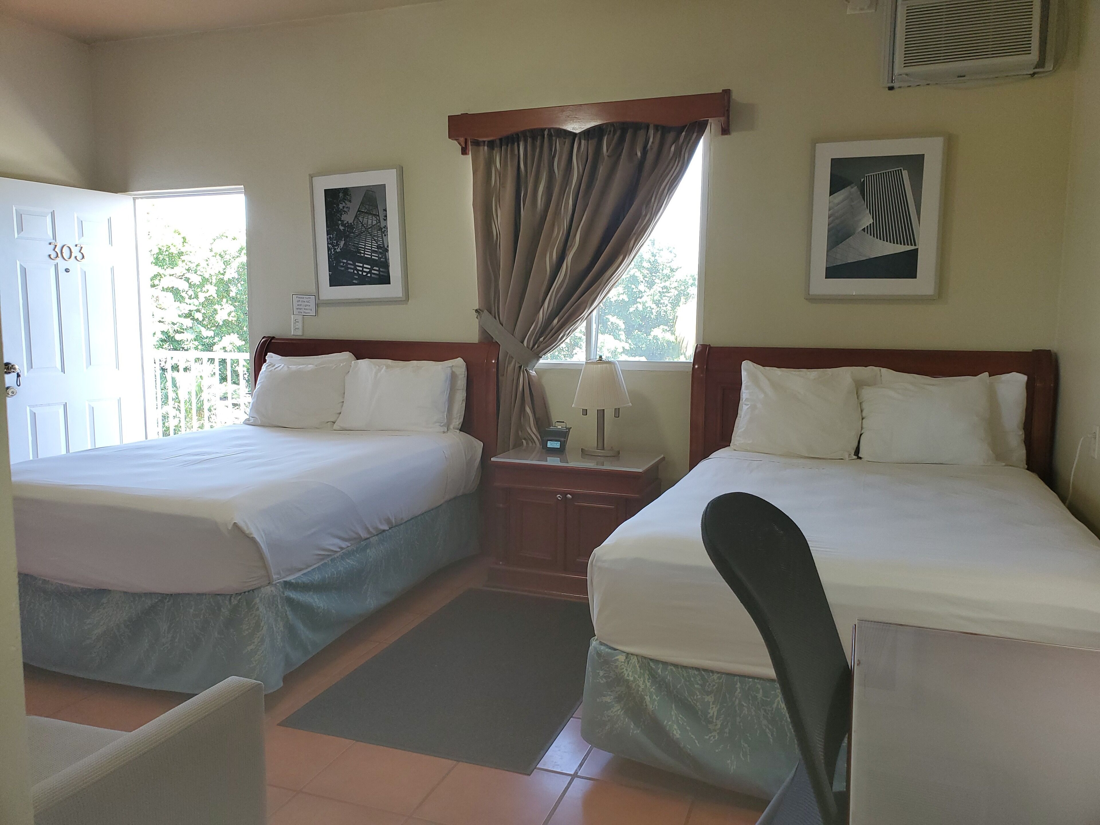 A hotel room with two beds, a desk, a chair, a window with curtains, and artwork on the walls.