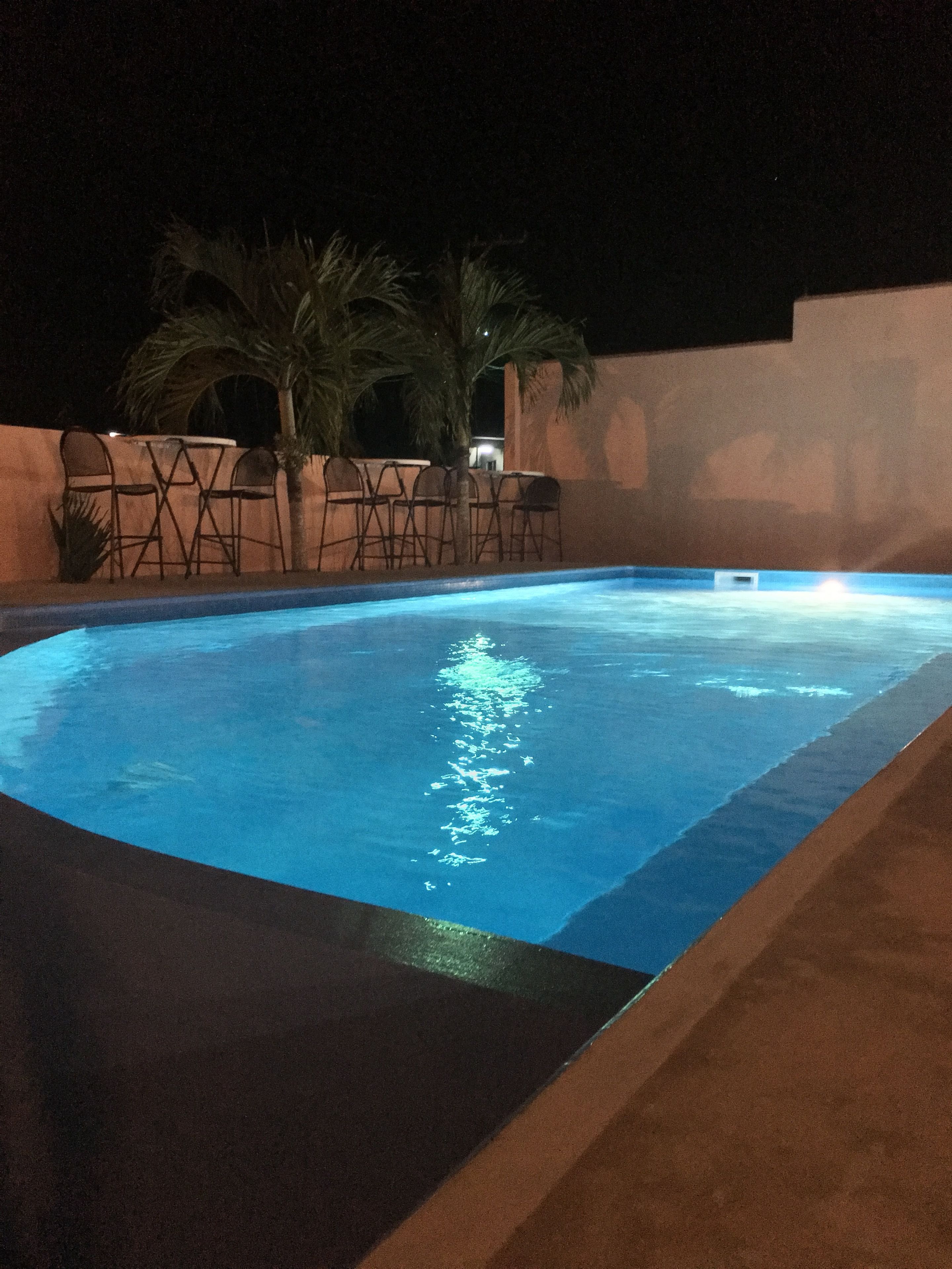 Una piscina nocturna con sillas y palmeras.