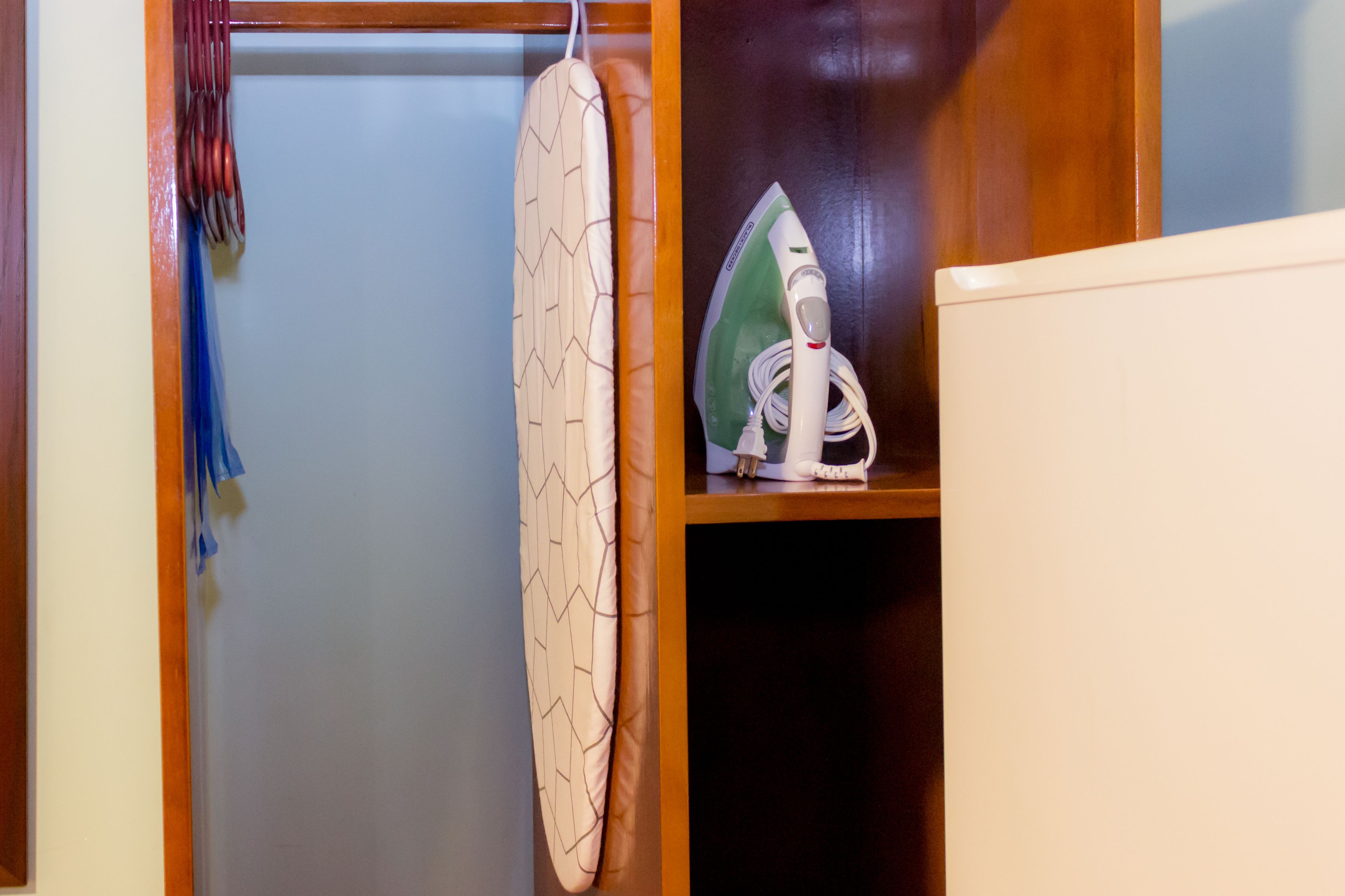 A closet with an ironing board, an iron, and a hanging garment.