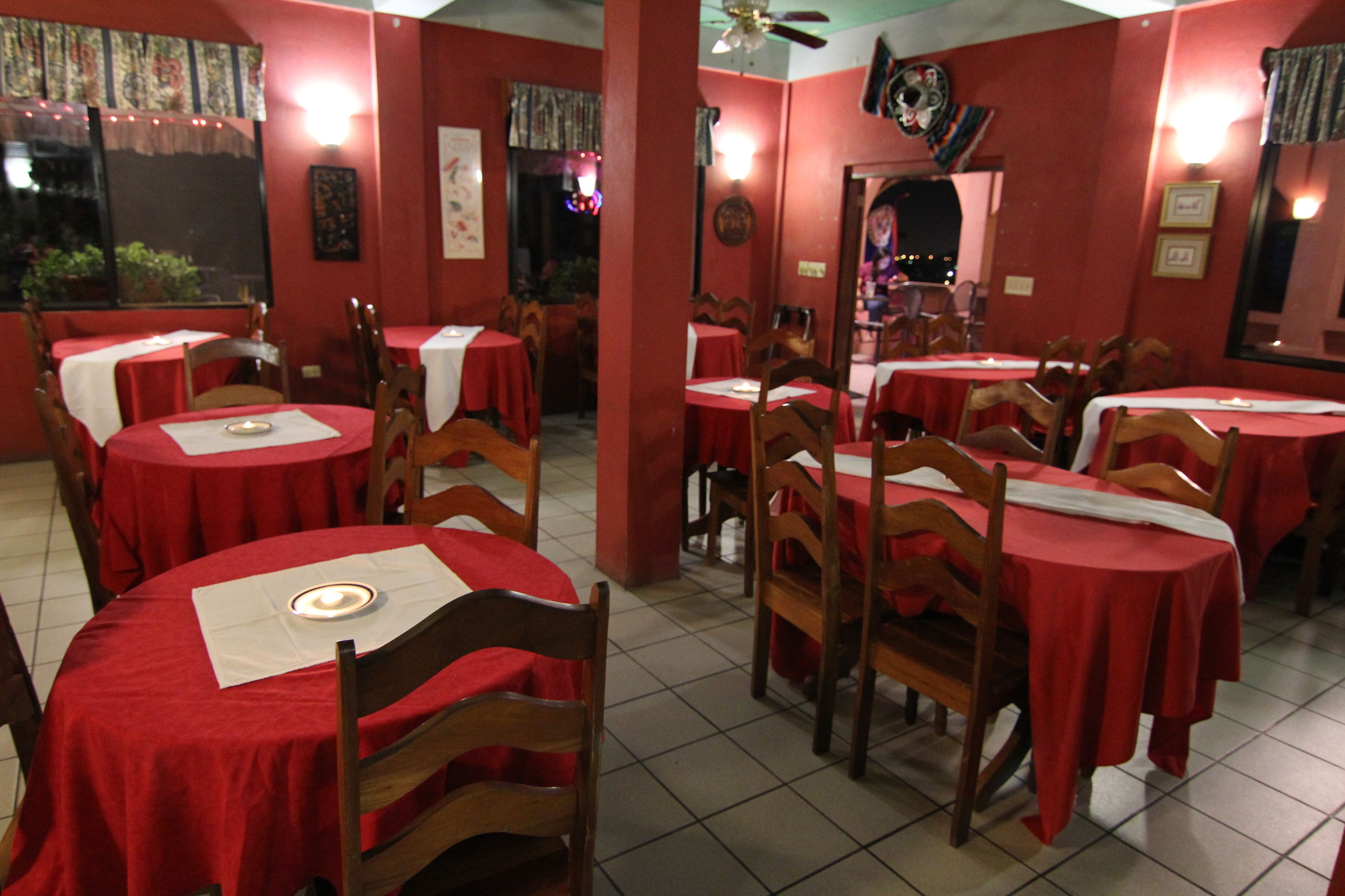 Un restaurant avec de nombreuses tables recouvertes de nappes rouges, des chaises en bois et un sol carrelé.