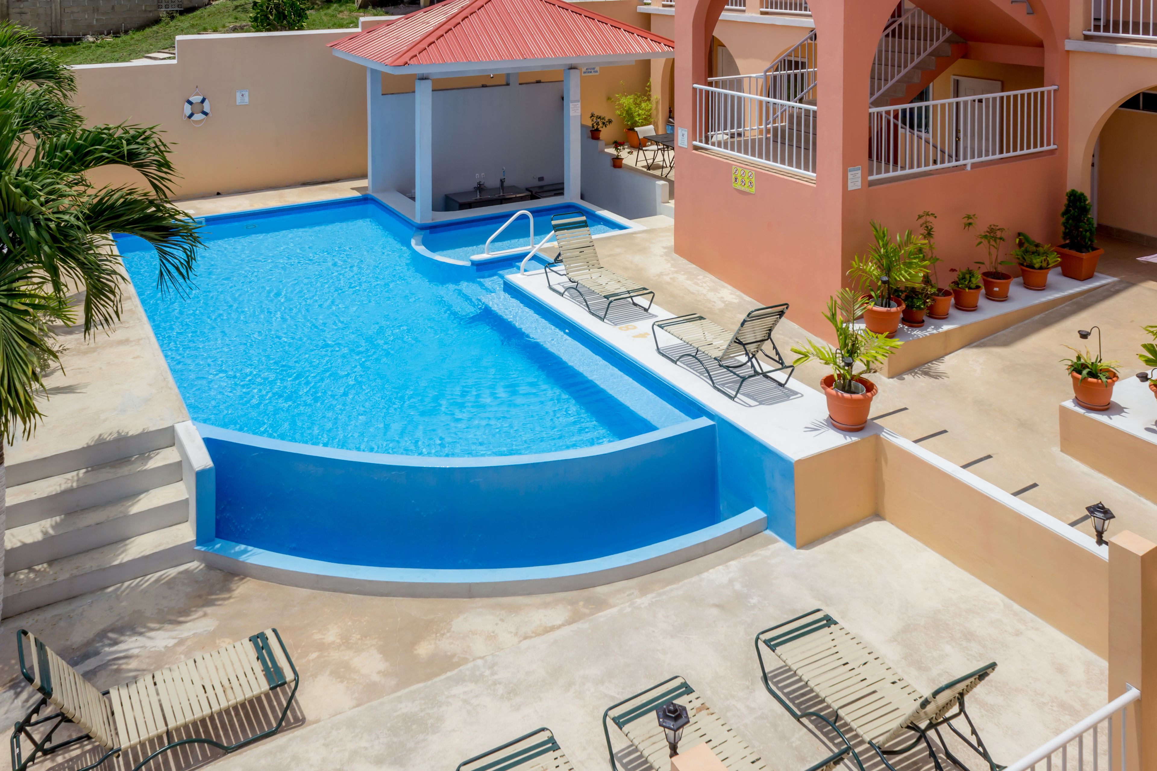 Una piscina con sillones de descanso, una zona cubierta y plantas en macetas.