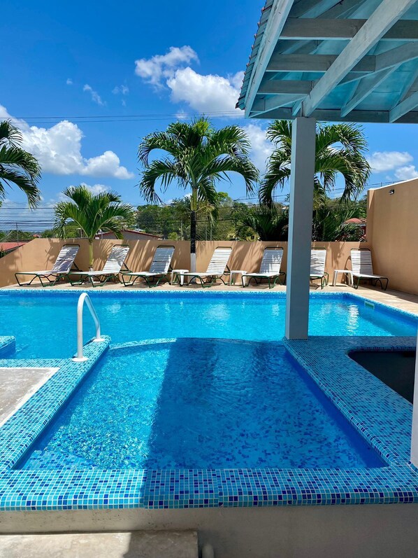 Una piscina al aire libre, sombrillas, sillones reclinables de piscina