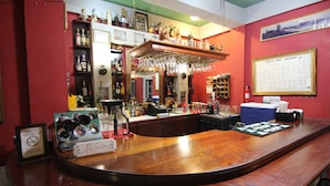 Un espace bar avec un comptoir en bois, des étagères remplies de bouteilles et un tableau périodique accroché au mur.