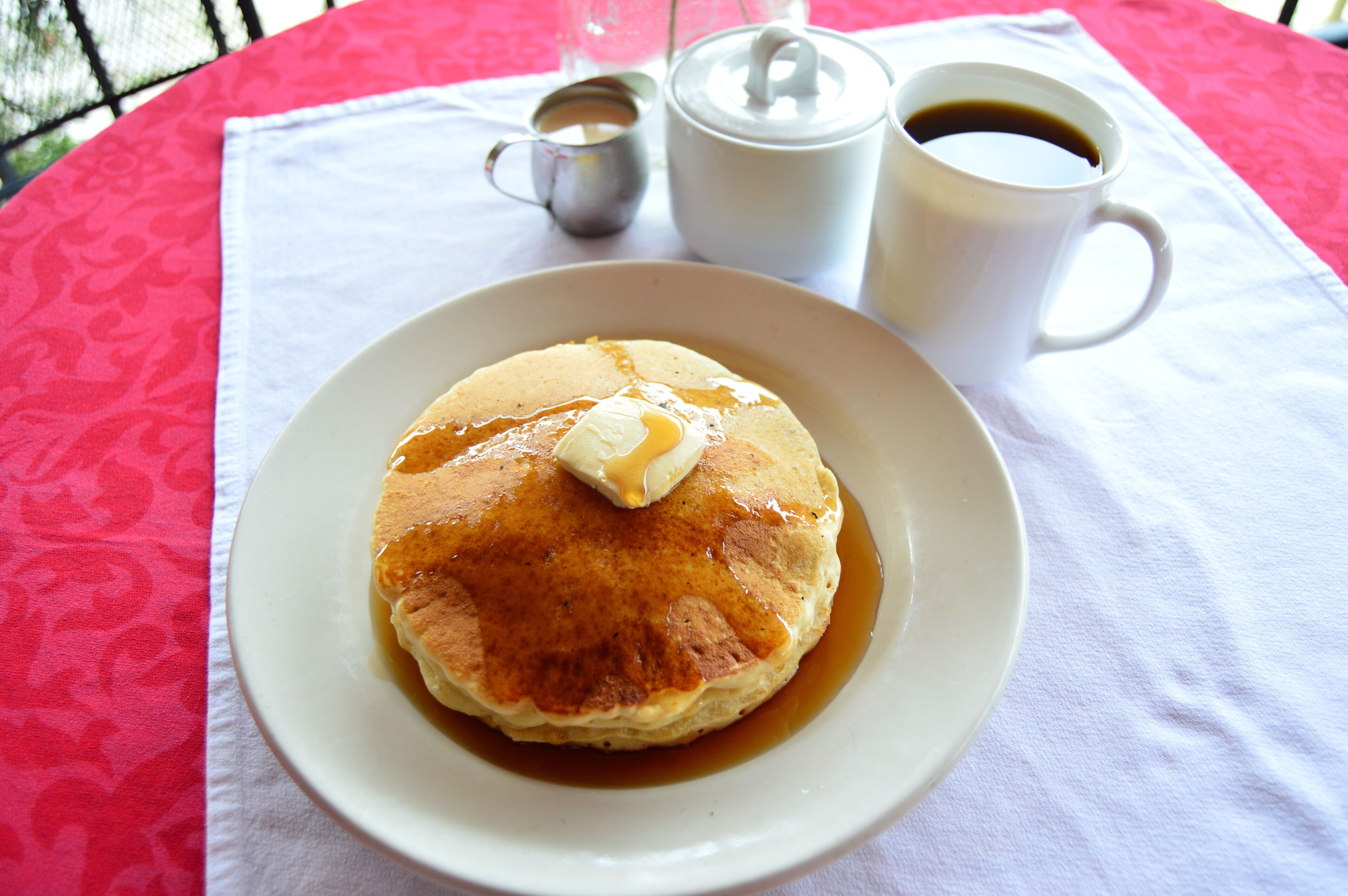 A plate of pancakes with syrup and butter on a table with a white tablecloth.
