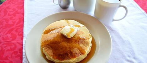 A plate of pancakes with syrup and butter on a table with a white tablecloth.
