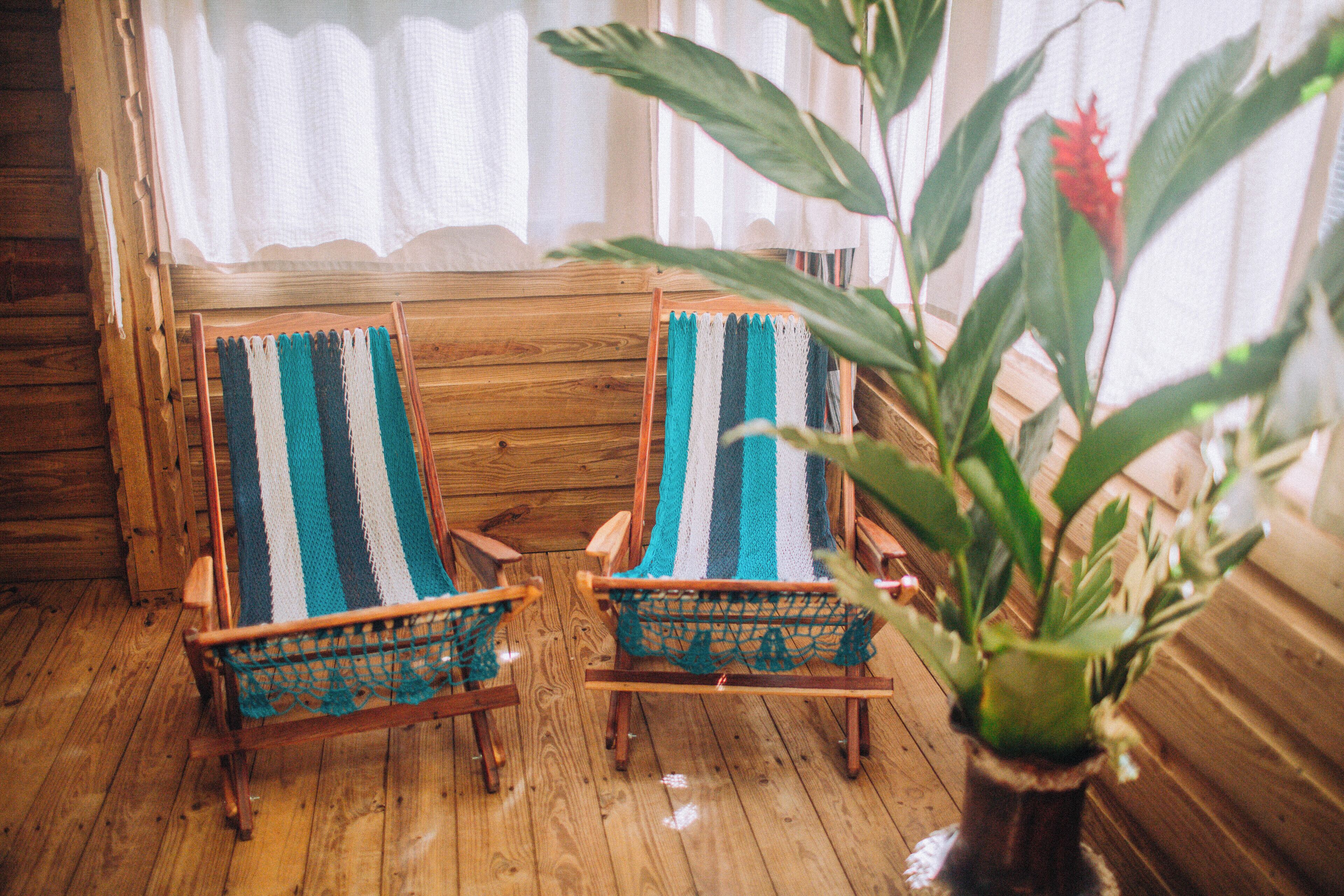 Two wooden rocking chairs with blue and white striped cushions, positioned in front of a wooden wall and a window with white curtains.