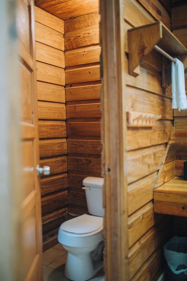 Un baño estilo cabaña de madera con inodoro, paredes de madera y un perchero para toallas.