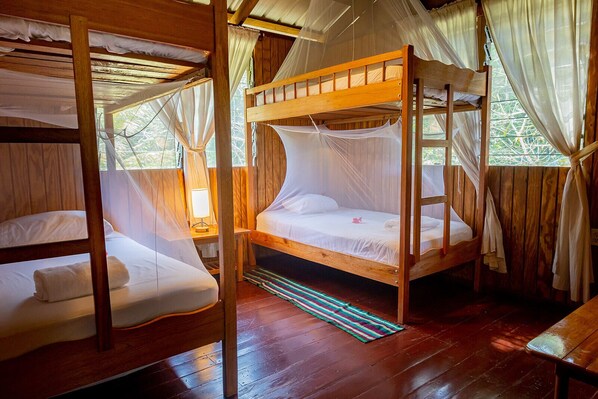 A wooden cabin with bunk beds, mosquito netting, and a small table with a lamp.