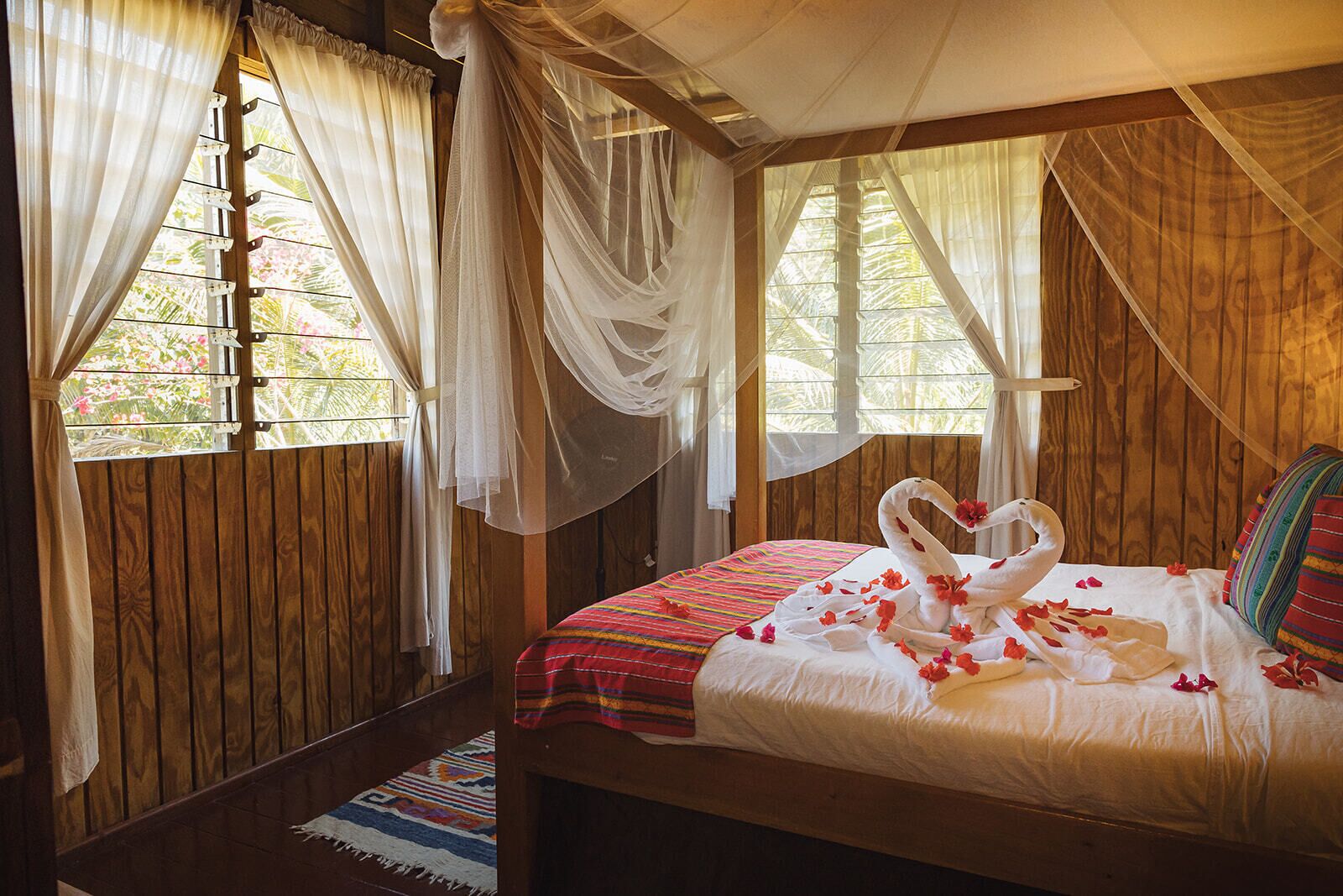 A wooden room with a bed, a window with curtains, and a view of greenery outside.
