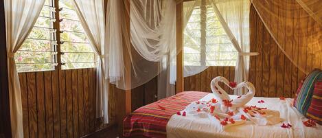 A wooden room with a bed, a window with curtains, and a view of greenery outside.