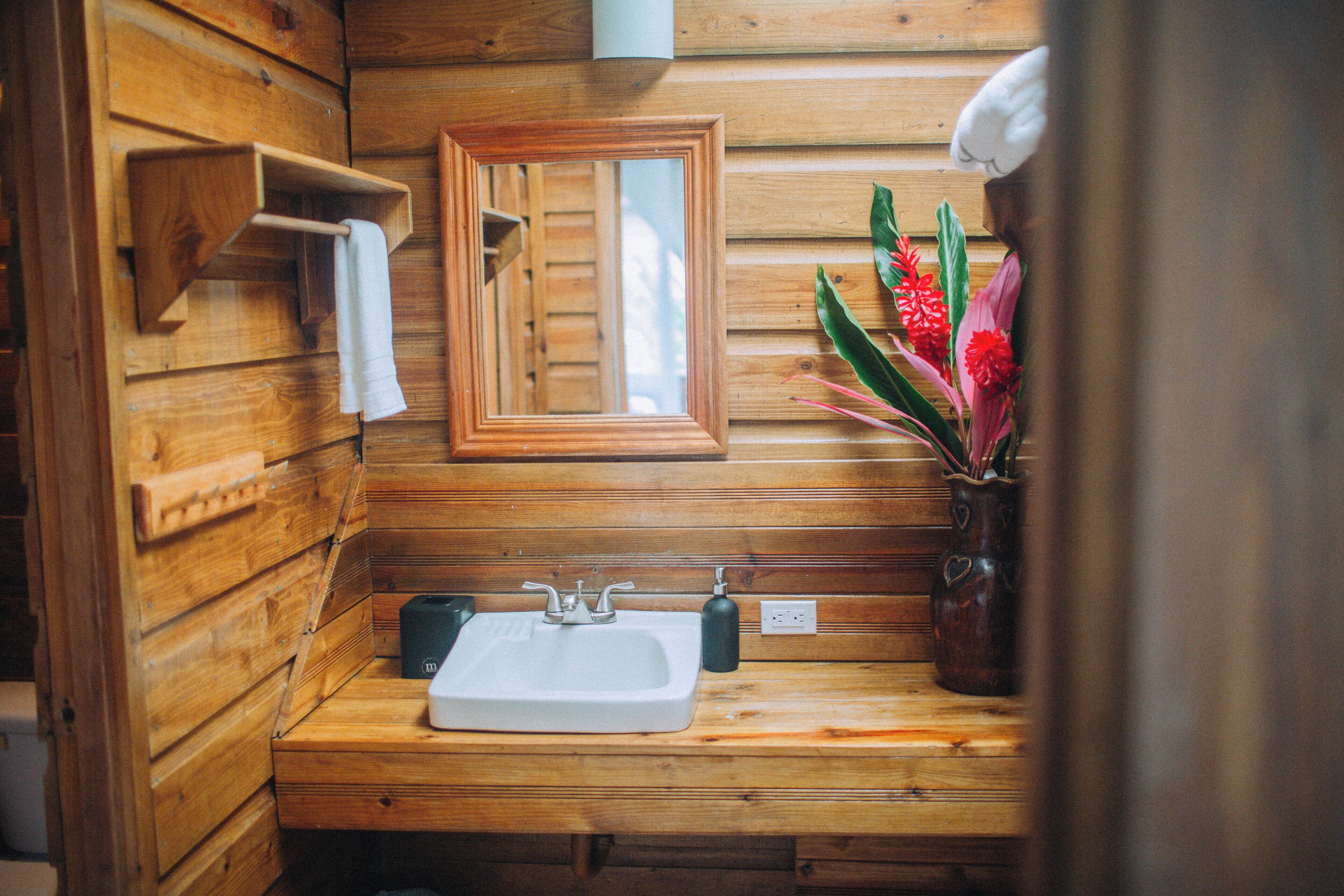Baño de cabaña de madera con lavamanos de madera, un espejo y un florero con flores.