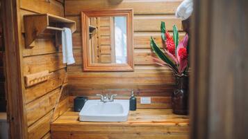 Baño de cabaña de madera con lavamanos de madera, un espejo y un florero con flores.