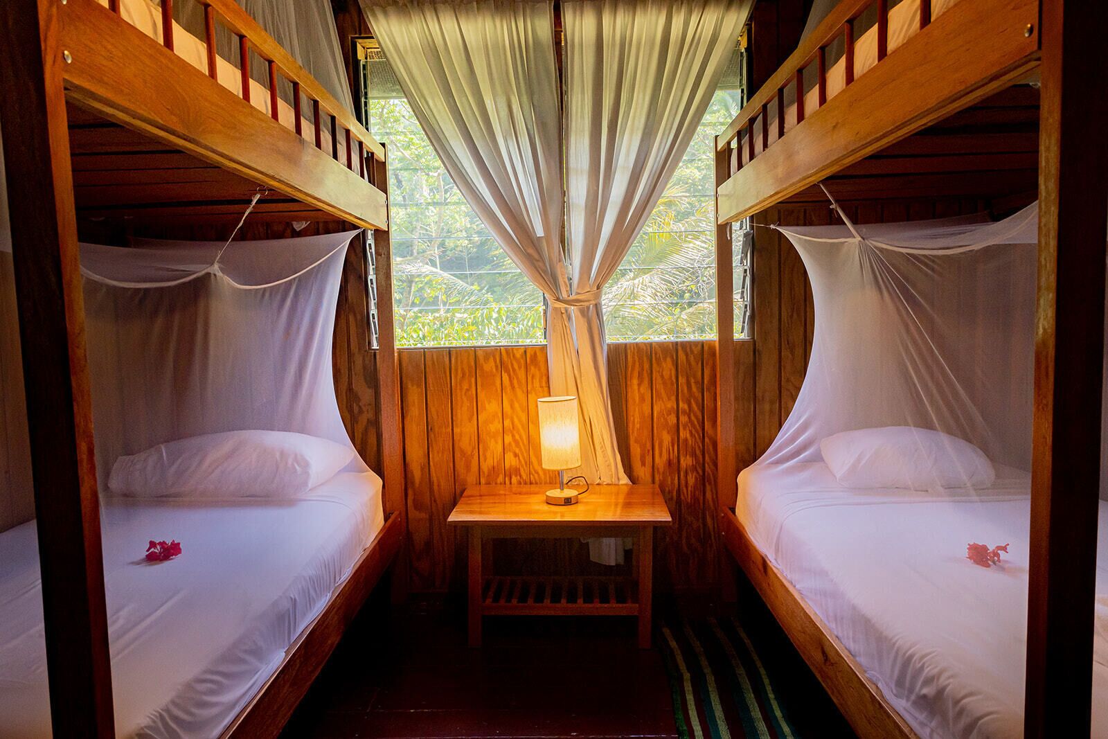 A room with two bunk beds, a small table with a lamp, and a window with curtains.
