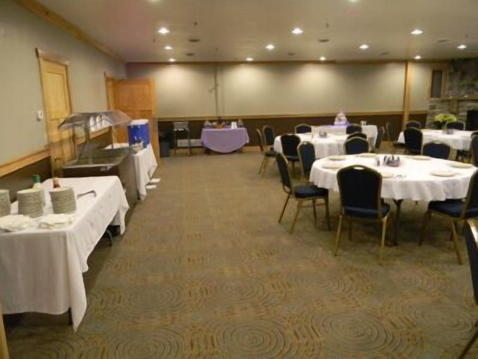 A banquet hall with round tables and chairs, a stage with a piano, and a buffet area.