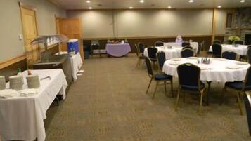 A banquet hall with round tables and chairs, a stage with a piano, and a buffet area.